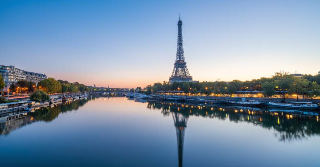 The Eiffel Tower at dusk, overlooking the Seine River in Paris, France, with city lights reflecting on the water.